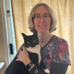 Female veterinarian with short blonde hair and glasses holding a black and white cat