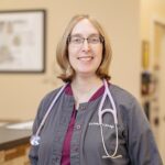Female veterinarian with short blonde hair and glasses holding a black and white cat