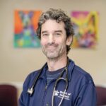 Male Veterinarian wearing a navy blue zip up jacket with practice logo and a stethoscope around his neck